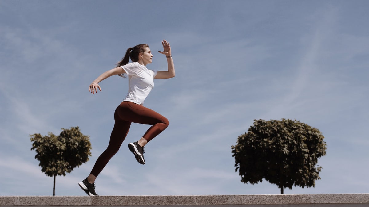 Athletic woman running on an outdoor road, demonstrating fitness and determination under a blue sky.